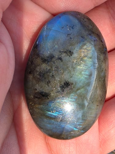Customer holding their iridescent monthly crystal, a labradorite palm stone, in their palm.