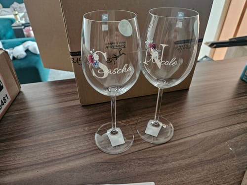 Rezensent zeigt zwei personalisierte Weingläser mit den Namen Sascha und Nicole und floralen Monogrammen.