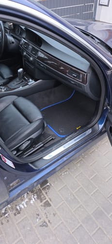 Recenzent pokazuje czarne dywaniki samochodowe z niebieskim obszyciem, idealnie dopasowane do podłogi pasażera.