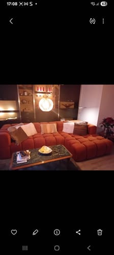 Recensent toont de oranje, gecapitonneerde Sky hoekbank in een sfeervolle woonkamer.