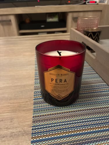 Recensent toont de Pera Geurkaars in de rode glazen houder, staand op een tafel.