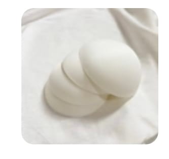 Close-up: Customer's four white Lovemère bra padding inserts stacked on a white fabric background.
