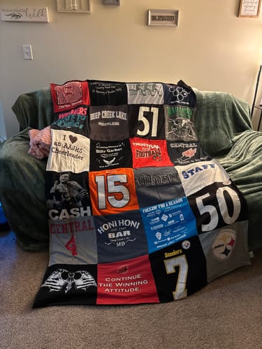 A customer's Premium T Shirt Quilt, made with various personal t-shirts, displayed on a green sofa.