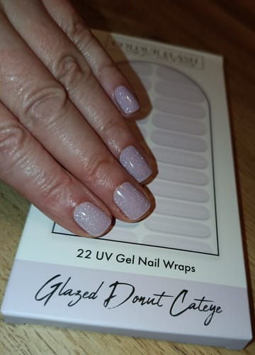 Eine Kundin zeigt ihre Maniküre mit den glitzernden Glazed Donut Cateye UV-Gel-Folien auf kurzen Nägeln.