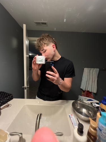 Reviewer taking a bathroom mirror selfie while holding and kissing a container of D-BLOAT.