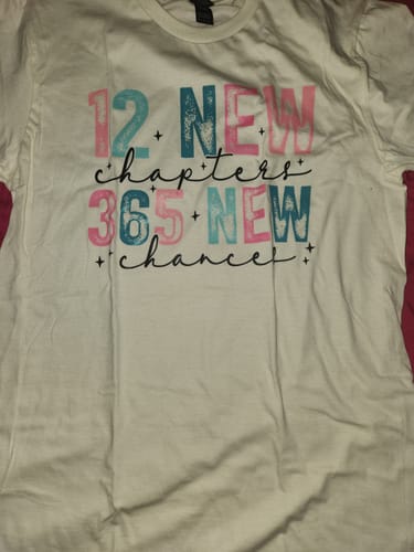 Customer's '12 New Chapters 365 New Chances' shirt laid flat, showing the pink and teal graphic on the front.