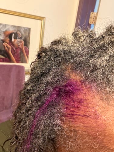 Close-up of a reviewer testing the purple Instant Dye Shampoo on a strand of grey curly hair.