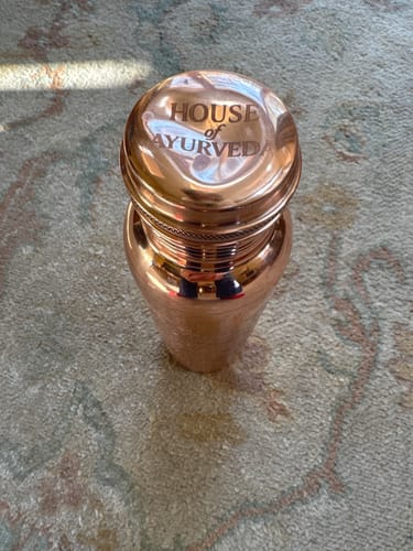 Customer's engraved copper water bottle with a large dent visible on its shiny cap.