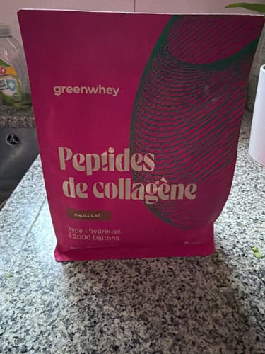Client montrant son sachet rose de Peptides de Collagène saveur chocolat sur un comptoir de cuisine.