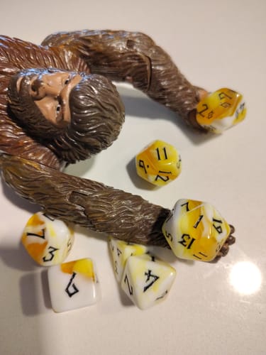 Reviewer's yellow and white marbled Movie Popcorn Acrylic Dice Set scattered around a brown toy figure on a white surface.