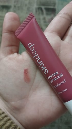 Reviewer holds the Peptide Lip Glaze in Roséwood, showing a glossy swatch on the palm of their hand.