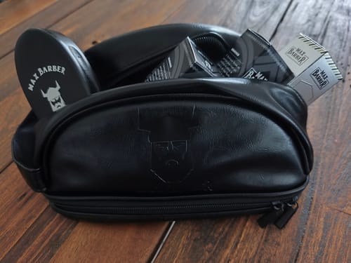 Un client montre sa Trousse Max-Barber® noire, remplie de produits de la marque et posée sur une surface en bois.