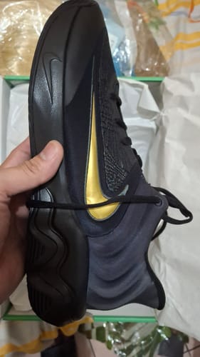 Customer holding a black Nike Giannis Immortality 4 EP basketball shoe with a prominent gold swoosh.