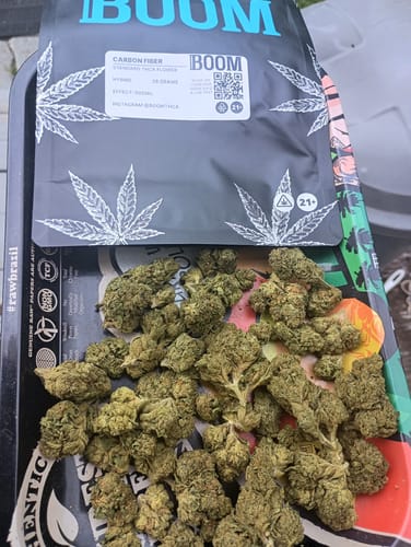 Customer's Fire OG cannabis buds spread out on a tray with the product's pouch in the background.