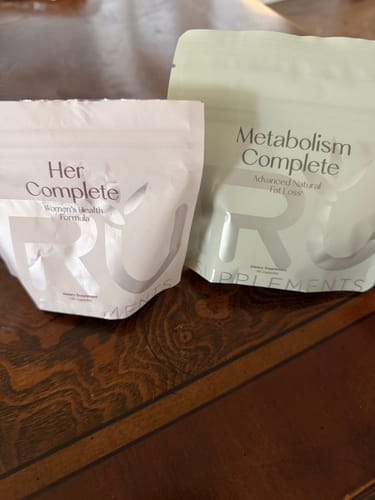 Reviewer's Her Complete women's supplement bag next to a bag of Metabolism Complete on a table.