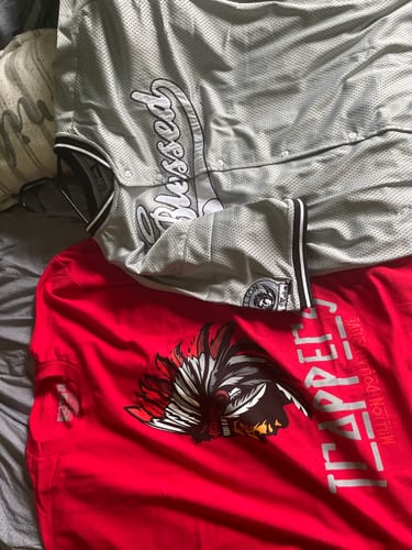 Customer's red Trappers T-shirt with a prominent graphic, laid out next to a gray jersey.