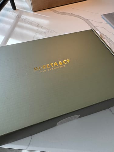 Packaging for the customer's M & Co. diamond stud earrings, a green box with gold lettering.