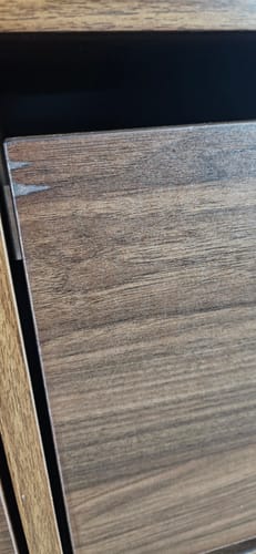 Close-up van een beschadigde hoek op het deurtje van het tv-meubel van de klant.