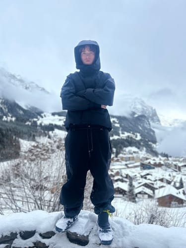 Reviewer wearing the oversized black snow pants while standing in a snowy mountain setting.