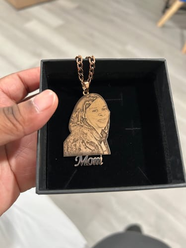 Customer showing a custom photo engraved pendant necklace in its gift box. The pendant has an engraved portrait and says 'Mom'.