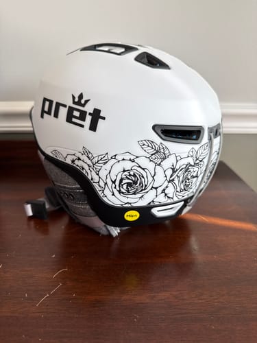 Customer's white Pret Vision MIPS Snow Helmet featuring a black-and-white rose graphic, sitting on a wooden table.