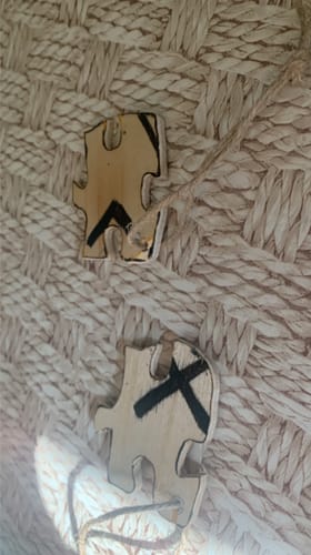 Customer's two wooden puzzle pieces with dark, abstract designs made with the Scorch Marker Pro against a woven surface.