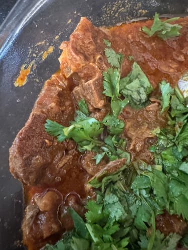 Close-up of a customer's cooked Halal Goat Loin Chops in a savory sauce, garnished with fresh cilantro in a clear dish.