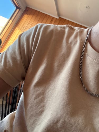 Primer plano de un cliente que lleva la Cadena Miami Cuban de 5mm sobre una camiseta de color beige.