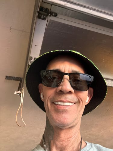 Customer smiling, showing their bright white Pop On Veneers while wearing sunglasses and a bucket hat.