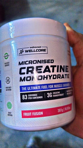 Customer's hand holding a white tub of Wellcore Micronised Creatine Monohydrate in Fruit Fusion flavor.