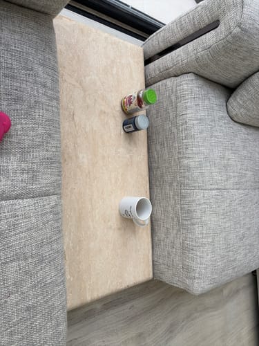 Customer's Quadro Sofa Side Table seen from above, placed between grey sofa cushions and holding a mug and jars.