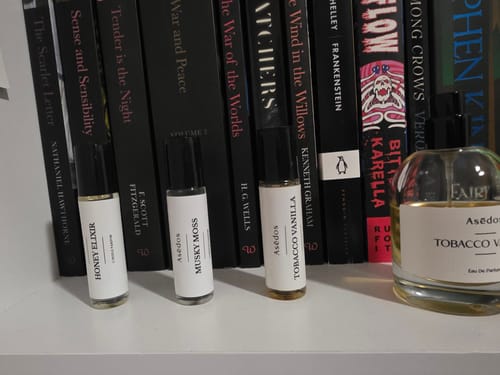 Customer's Honey Elixir Perfume Oil bottle on a shelf with other fragrances in front of a row of books.