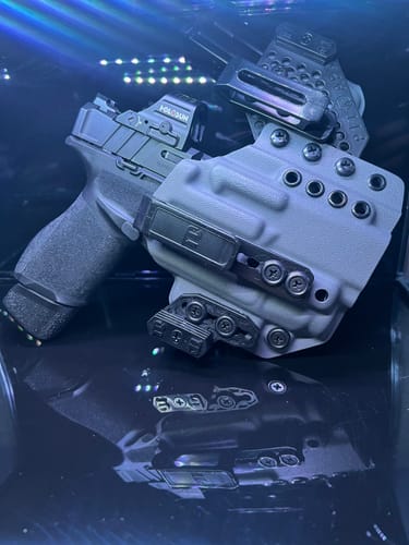 Customer's light gray APX holster with a handgun and attached magazine carrier, on a reflective surface.