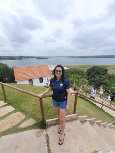 Avaliadora usando os Óculos Tropea Edição Limitada em uma escadaria ao ar livre com vista para o mar.