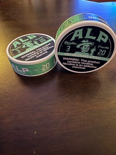 Reviewer's two tins of Refreshing Chill Nicotine Pouches, one flat and one on its side, on a wooden table.