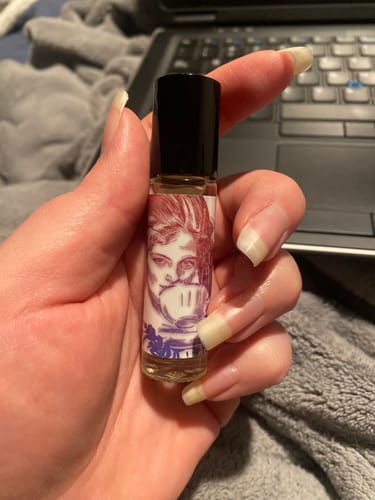 Customer's hand holding the Victoriana perfume rollerball, showing the detailed, illustrated label.