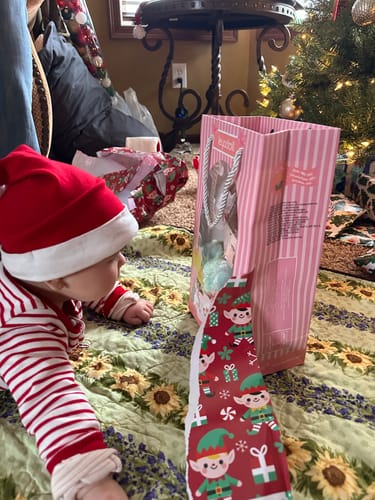 Reviewer's photo of a baby in a Santa hat next to a gift bag for the Personalized Meadow Girl doll.