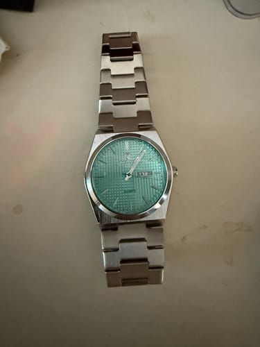 Reviewer's Lucky Fours® Jaxon watch with a silver band and textured light green face, laid flat.