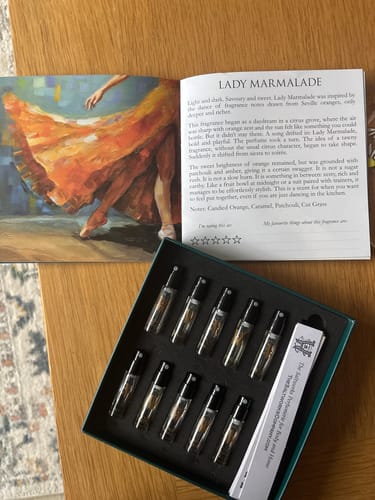 Customer's open Discovery Set box with perfume vials next to a descriptive booklet on a wooden table.