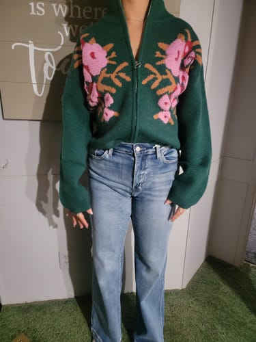 Customer wearing the Tori Floral Zip Up Sweater, showing its green color and bold floral print.