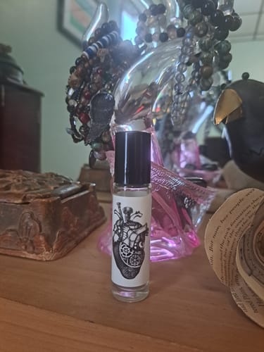 Customer's Heavy Heart perfume oil in a roll-on bottle with a mechanical heart on the label, placed on a wooden surface.
