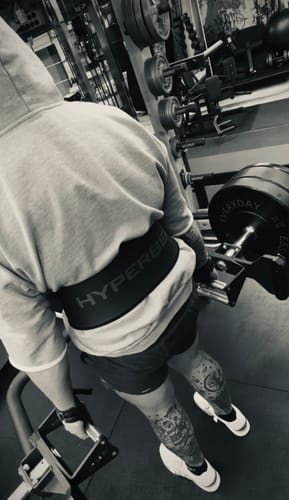 Reviewer wearing the Megàlo 3/5 Sleeve Hoodie from behind in a gym, showing it bunched up above their waist.