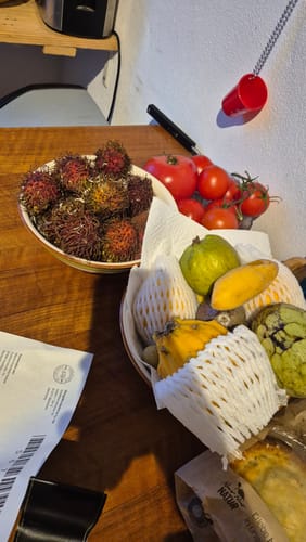 Ein Kunde zeigt seine 'Exotische Früchte' Probierbox mit frischen Rambutans, Pitaya und Cherimoya auf einem Holztisch.