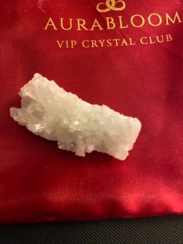 Customer's white crystal cluster from the VIP Crystal Club resting on its red branded pouch.