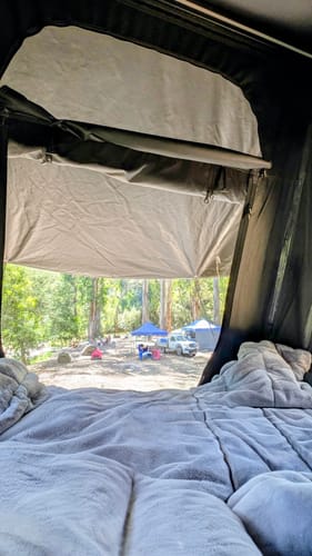 Reviewer's grey Ultra Warm Comforter Blanket on a bed inside a tent, overlooking a campsite.