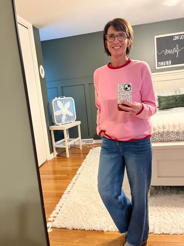 Reviewer wearing the pink Sweet & Simple Contrast Sweater with blue jeans in a bedroom.