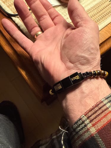 Close-up of a reviewer's wrist wearing a beaded bracelet with a black clasp and flag detail.