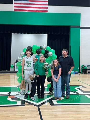 Reviewer wearing the green Luxe Ease Long Sleeve Blouse with her family at a school basketball event.