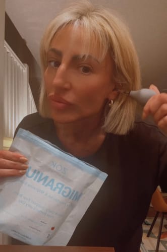 Reviewer holds a pouch of Migranium drink mix and uses a pressure relief tool near their ear.