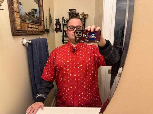 Reviewer taking a mirror selfie wearing the red 'Lil Muppets' KUNUFLEX shirt layered over a dark long-sleeve top.